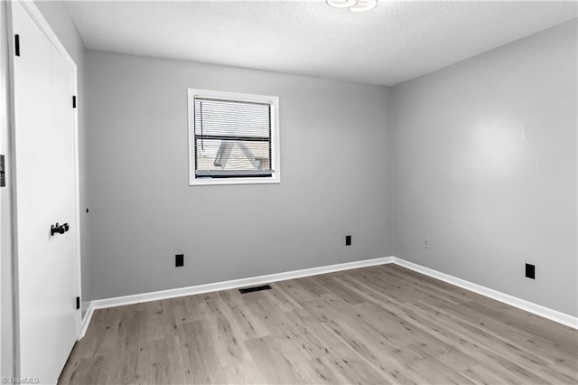 spare room with a textured ceiling, visible vents, light wood finished floors, and baseboards