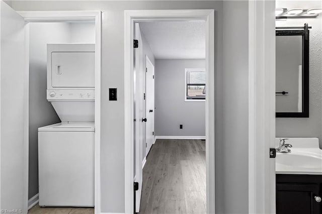 washroom with stacked washer / drying machine, laundry area, a sink, baseboards, and light wood-style flooring