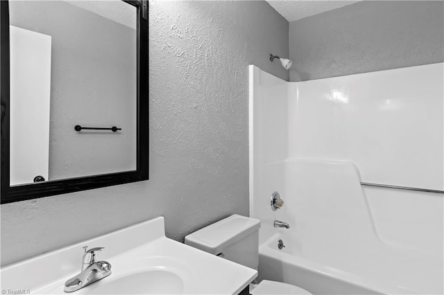 full bathroom with a textured ceiling, toilet, washtub / shower combination, a textured wall, and vanity
