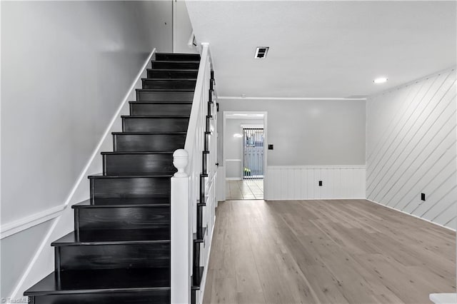 staircase featuring wood finished floors and a wainscoted wall