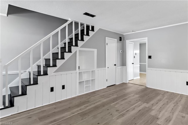stairs featuring wood finished floors, a textured ceiling, and wainscoting