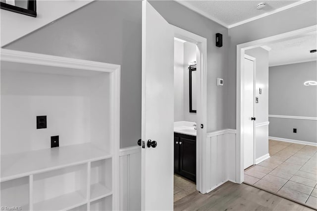 hallway featuring light wood-style flooring, a textured ceiling, and a wainscoted wall