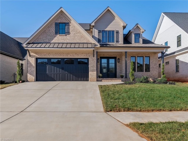 view of front facade featuring brick siding, a porch, a standing seam roof, driveway, and a front lawn