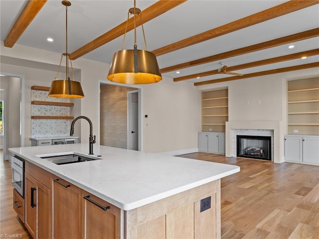 kitchen featuring decorative light fixtures, light wood finished floors, open shelves, a kitchen island with sink, and a sink