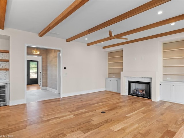 unfurnished living room with built in shelves, a high end fireplace, light wood-type flooring, beamed ceiling, and baseboards