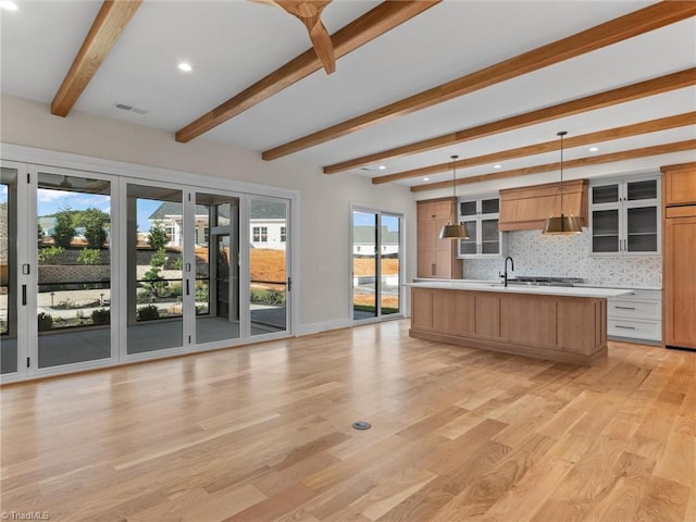 kitchen with light wood finished floors, tasteful backsplash, a center island with sink, light countertops, and pendant lighting