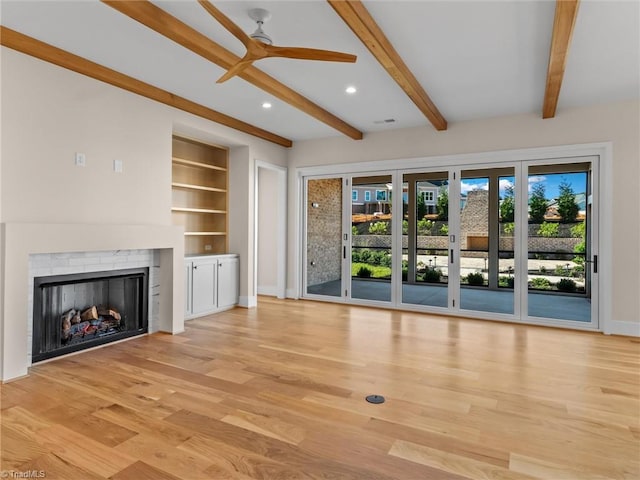 unfurnished living room with built in shelves, a fireplace, a ceiling fan, light wood-type flooring, and baseboards