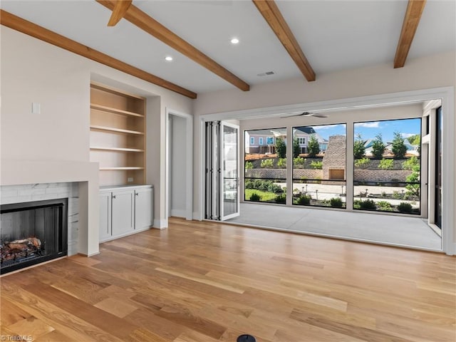 unfurnished living room with built in features, beam ceiling, a fireplace, visible vents, and light wood-style floors