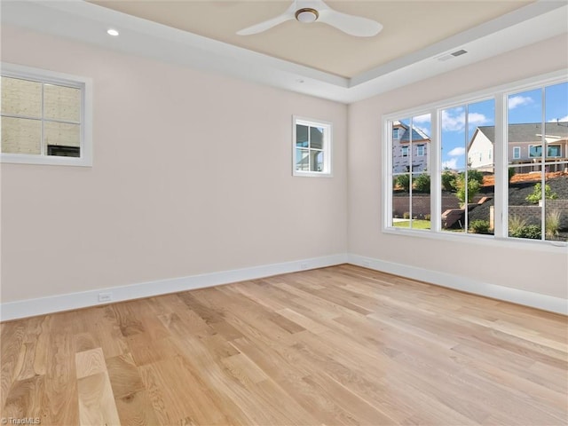 unfurnished room with visible vents, a tray ceiling, light wood-style flooring, and baseboards