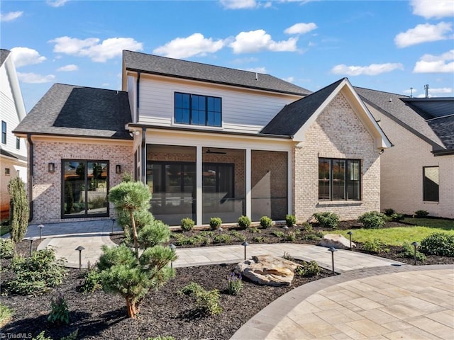 back of house featuring a patio, brick siding, roof with shingles, and a sunroom