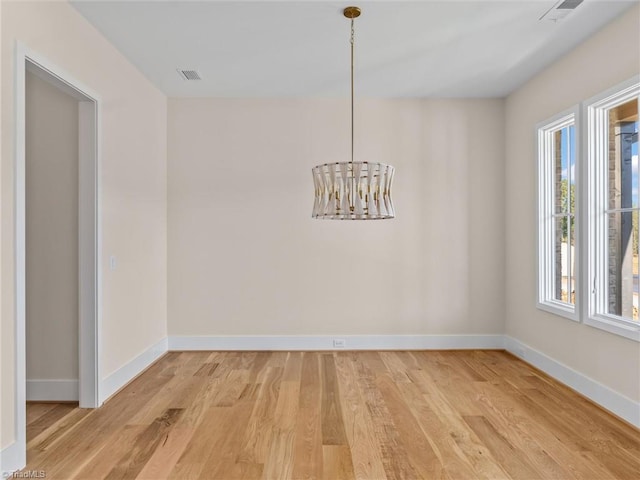 unfurnished dining area with light wood-type flooring, visible vents, baseboards, and an inviting chandelier