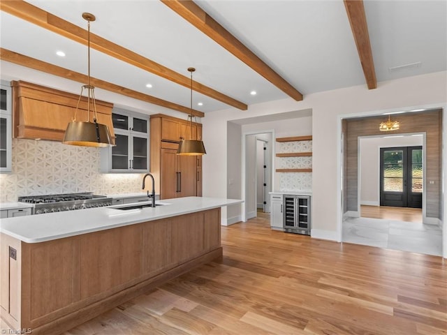 kitchen with decorative light fixtures, open shelves, light countertops, a sink, and an island with sink