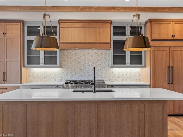 kitchen featuring paneled built in fridge, an island with sink, light countertops, and decorative light fixtures