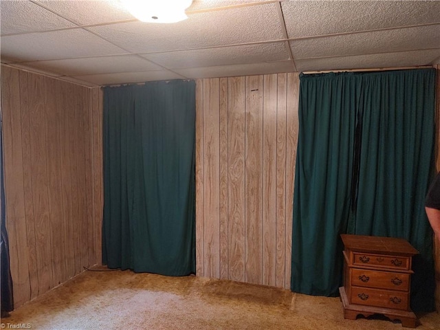 unfurnished bedroom featuring carpet, a paneled ceiling, and wooden walls