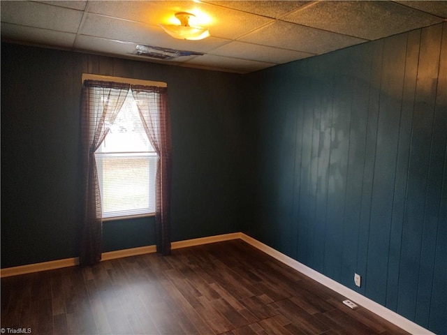 unfurnished room with hardwood / wood-style flooring, a drop ceiling, and wood walls