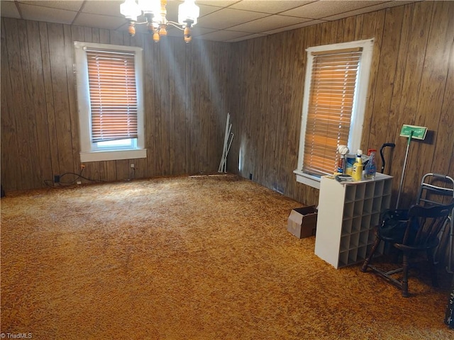 empty room with a paneled ceiling, wooden walls, carpet, and a chandelier