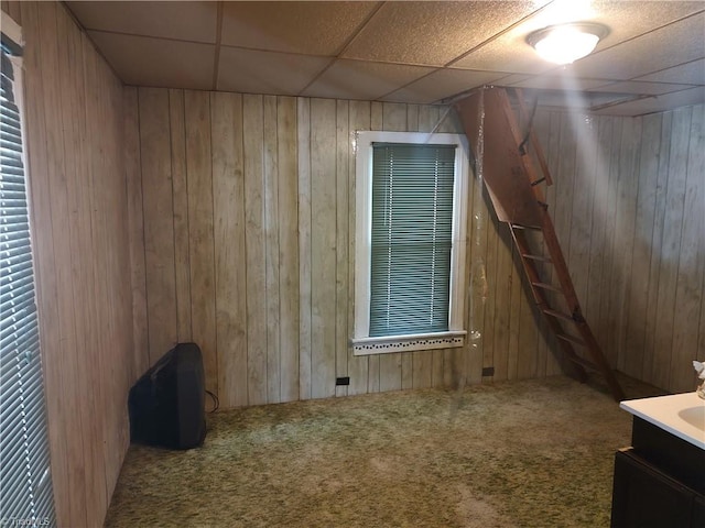 carpeted empty room with a paneled ceiling and wood walls