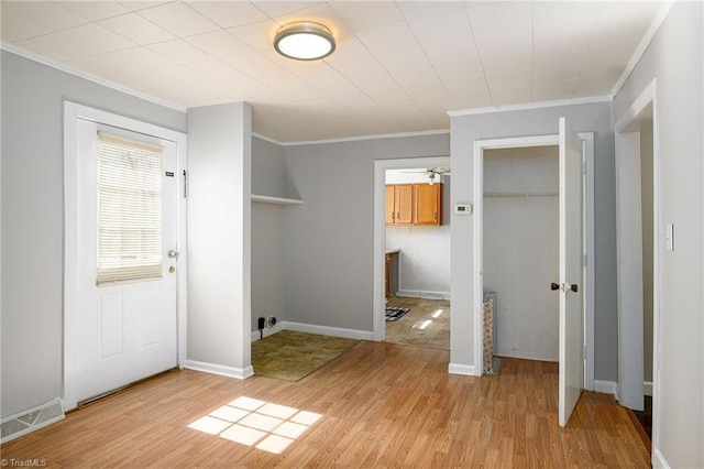 interior space with light wood-style floors, baseboards, visible vents, and crown molding