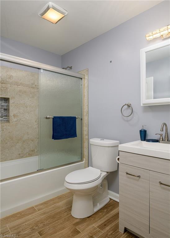 full bathroom with toilet, shower / bath combination with glass door, wood finished floors, and vanity