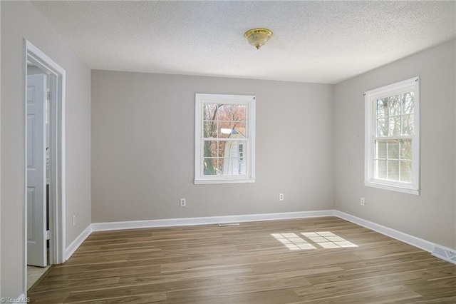 empty room with a textured ceiling, wood finished floors, and baseboards