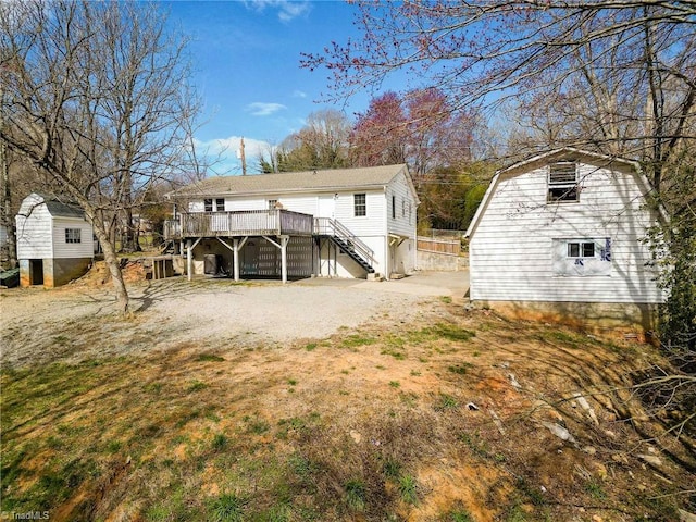 back of house featuring driveway, stairway, an outdoor structure, and a wooden deck