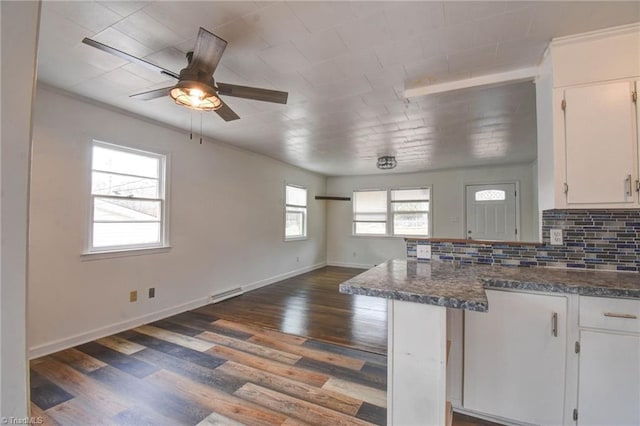 kitchen with dark wood-type flooring, dark stone countertops, backsplash, white cabinets, and kitchen peninsula