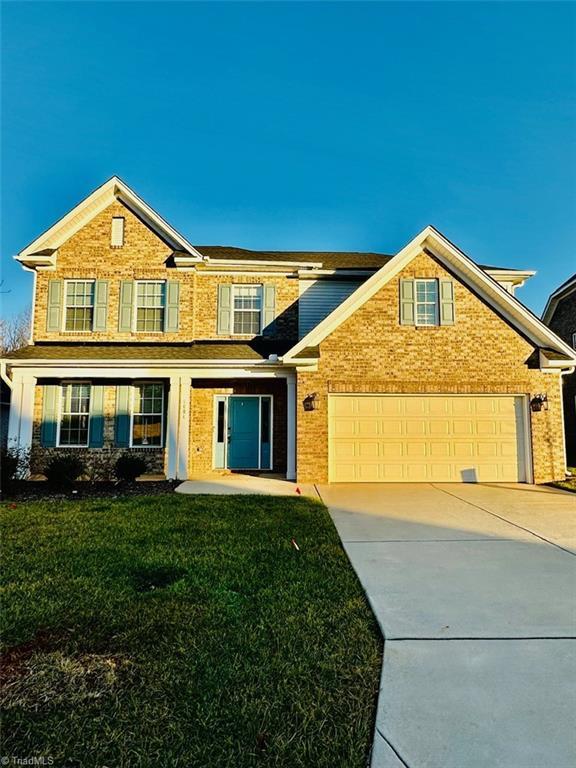 traditional home featuring driveway, brick siding, a garage, and a front yard