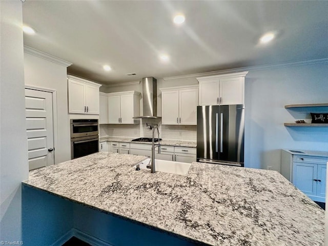 kitchen featuring decorative backsplash, appliances with stainless steel finishes, white cabinets, a sink, and wall chimney exhaust hood