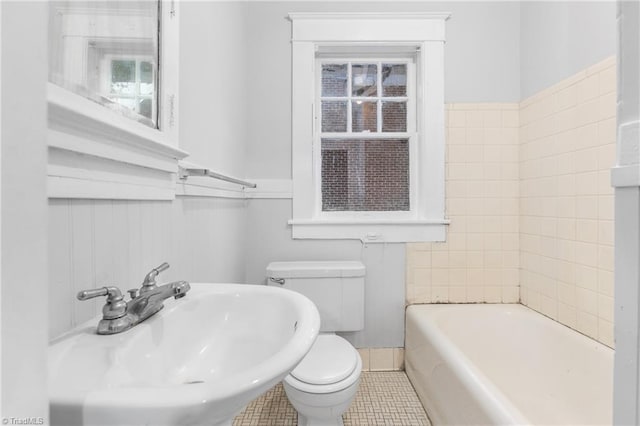 bathroom featuring toilet, plenty of natural light, a bath, and sink