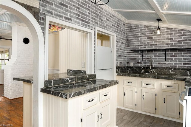 kitchen with dark wood-type flooring, white appliances, ornamental molding, dark stone countertops, and brick wall