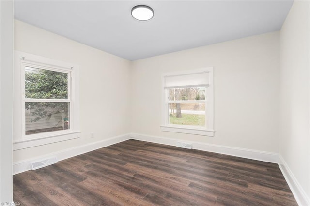 spare room with dark wood finished floors, visible vents, and a wealth of natural light