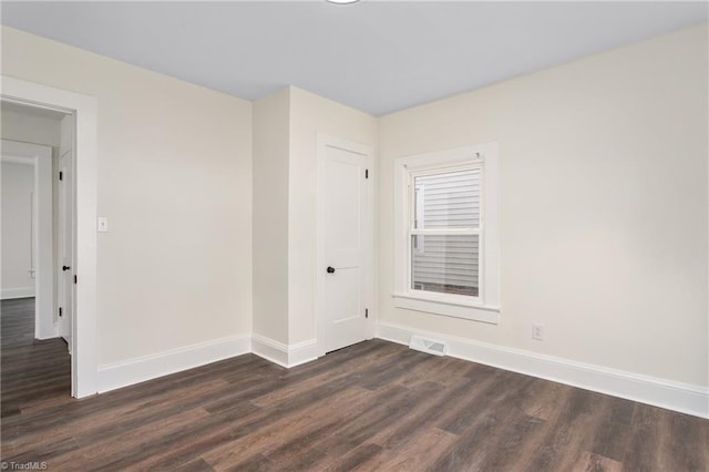 spare room featuring dark wood finished floors, visible vents, and baseboards