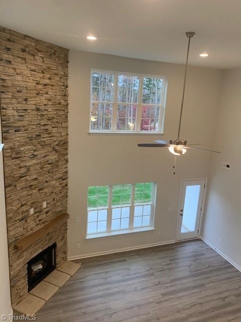 unfurnished living room featuring ceiling fan, a stone fireplace, and wood-type flooring