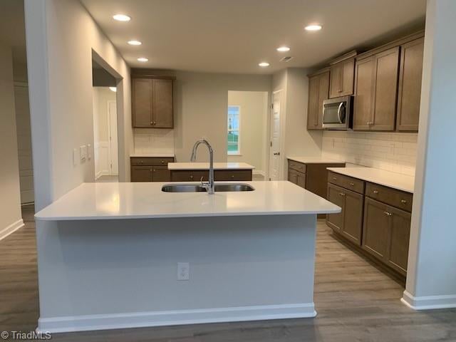 kitchen with hardwood / wood-style floors, backsplash, an island with sink, and sink