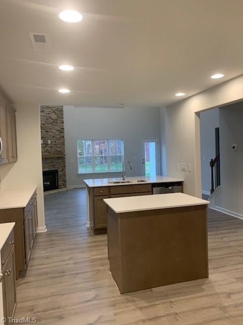 kitchen featuring a fireplace, sink, a kitchen island with sink, and light hardwood / wood-style flooring