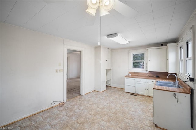 kitchen with butcher block counters, sink, white cabinets, and ceiling fan