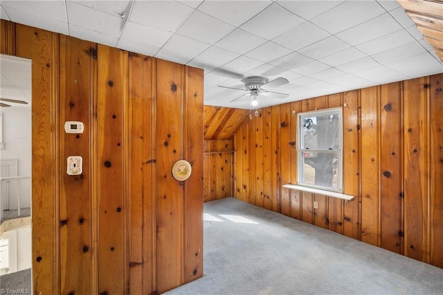 additional living space featuring carpet floors, wooden walls, and ceiling fan