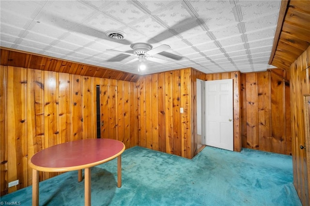 unfurnished room with carpet floors, wooden walls, and ceiling fan