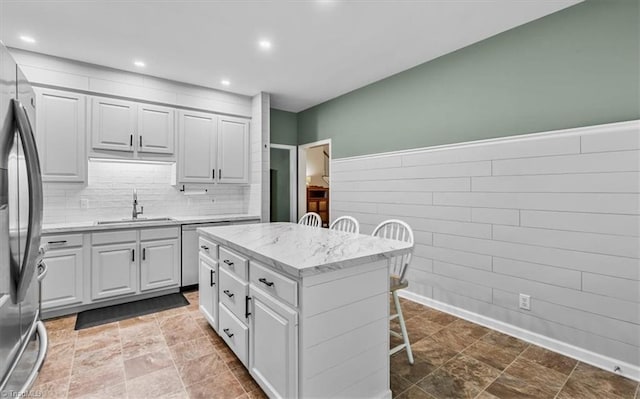 kitchen featuring freestanding refrigerator, a breakfast bar, recessed lighting, light stone counters, and a sink
