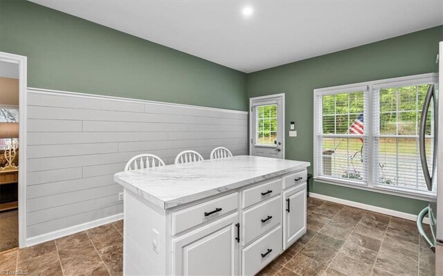 kitchen featuring stainless steel fridge, baseboards, white cabinets, and a kitchen island