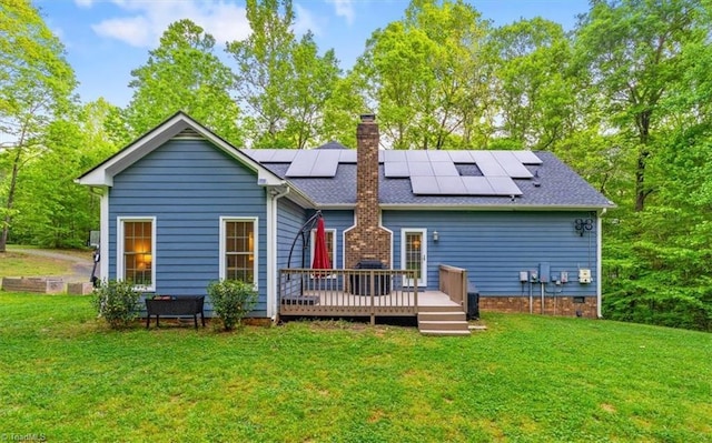 back of property with a lawn, a wooden deck, a chimney, and roof mounted solar panels