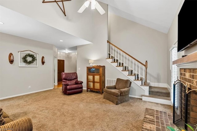 carpeted living area with a ceiling fan, visible vents, a fireplace, stairway, and high vaulted ceiling