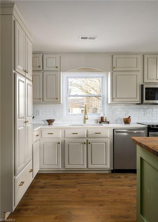 kitchen with butcher block counters, sink, tasteful backsplash, appliances with stainless steel finishes, and dark hardwood / wood-style flooring