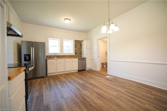 kitchen featuring wood-type flooring, stainless steel appliances, white cabinets, range hood, and a chandelier