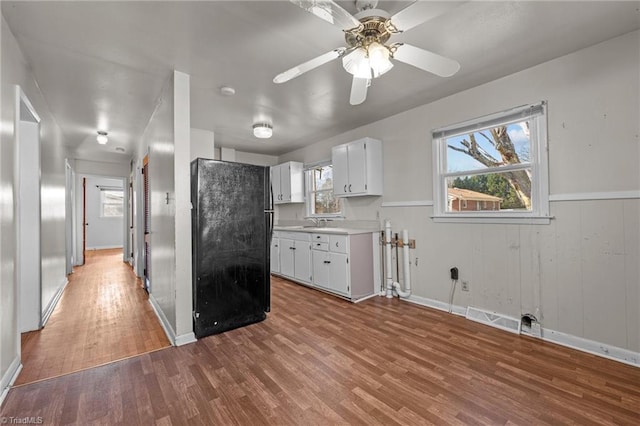 kitchen featuring white cabinets, black refrigerator, sink, hardwood / wood-style flooring, and ceiling fan