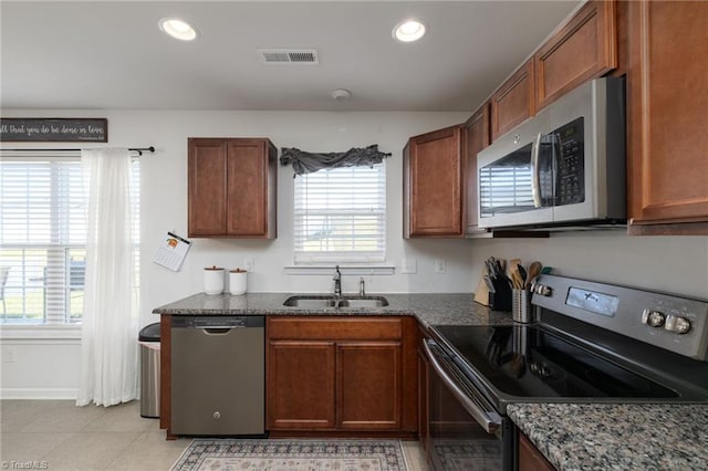 kitchen with appliances with stainless steel finishes, a wealth of natural light, dark stone counters, and sink