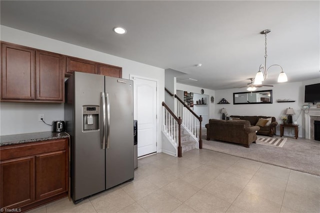 kitchen with ceiling fan, a tile fireplace, decorative light fixtures, dark stone countertops, and stainless steel fridge with ice dispenser