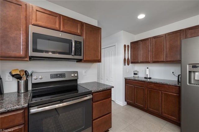 kitchen featuring light tile patterned floors, stainless steel appliances, and dark stone counters