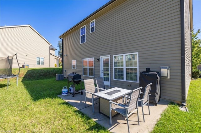 back of house with a trampoline, central AC, a patio area, and a lawn