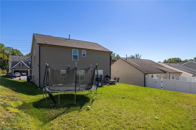 back of house featuring a trampoline and a yard